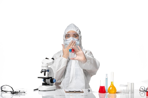 Front view young female doctor in white protective suit with mask due to covid holding empty flasks on the white background pandemic splash virus covid-