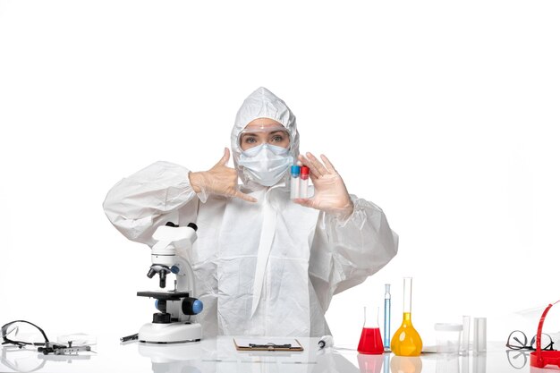 Front view young female doctor in white protective suit with mask due to covid holding flasks on light-white background pandemic splash virus health covid