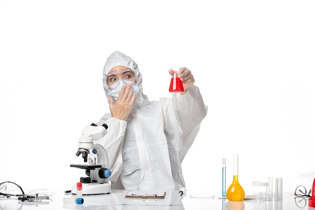 Front view young female doctor in white protective suit with mask due to covid holding red solution on the white background virus pandemic splash covid-