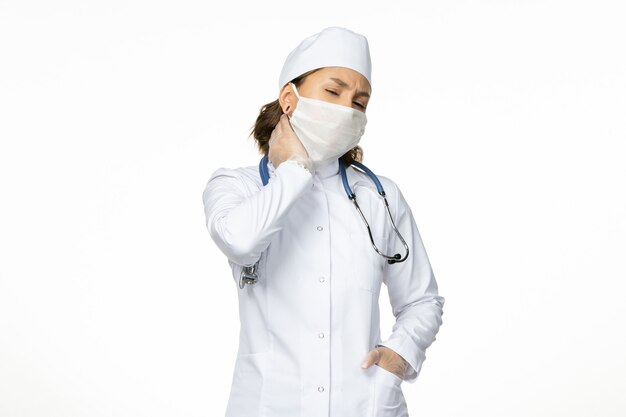 Front view young female doctor with sterile mask and gloves due to coronavirus having neckache on white surface