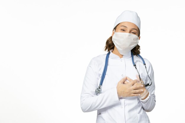 Front view young female doctor with sterile mask and gloves due to coronavirus on the light white surface