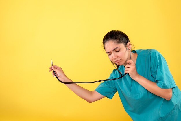 Front view of young female doctor with stethoscope on yellow wall