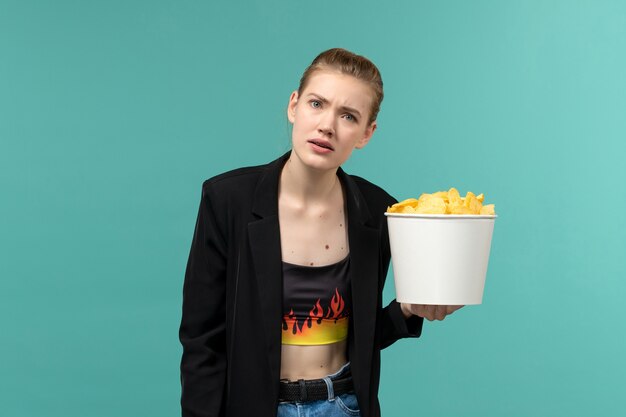 Front view young female eating potato chips and watching movie on blue desk