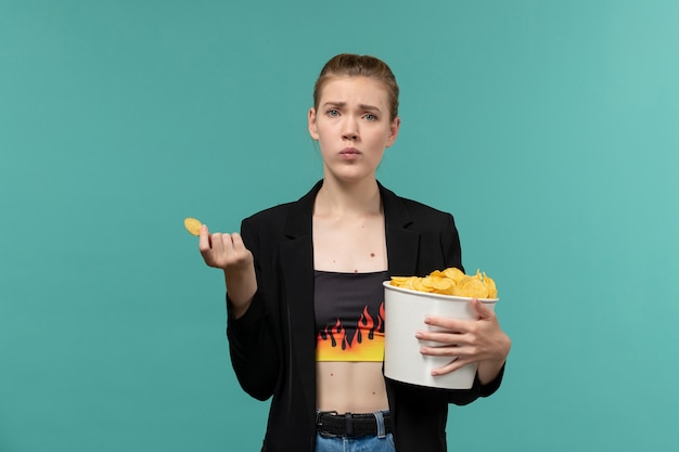 Free photo front view young female eating potato chips and watching movie on light blue surface