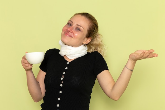 Front view young female feeling very ill and sick holding cup of coffee on light green wall sickness medicine illness