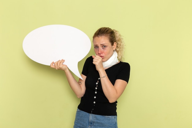 Free photo front view young female feeling very ill and sick holding huge white sign coughing on the green wall sickness medicine health illness