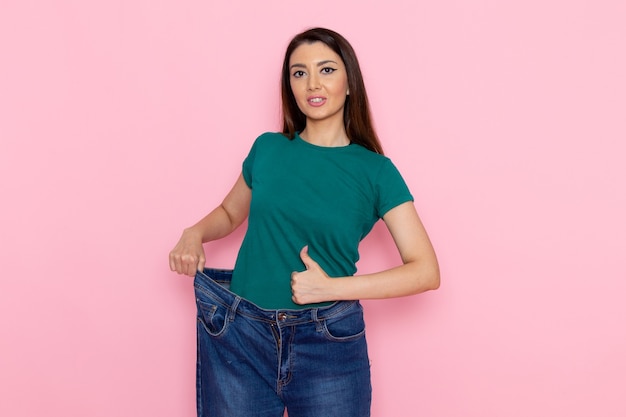 Free photo front view young female in green t-shirt checking her waist on the pink wall waist sport exercise workouts beauty slim athlete