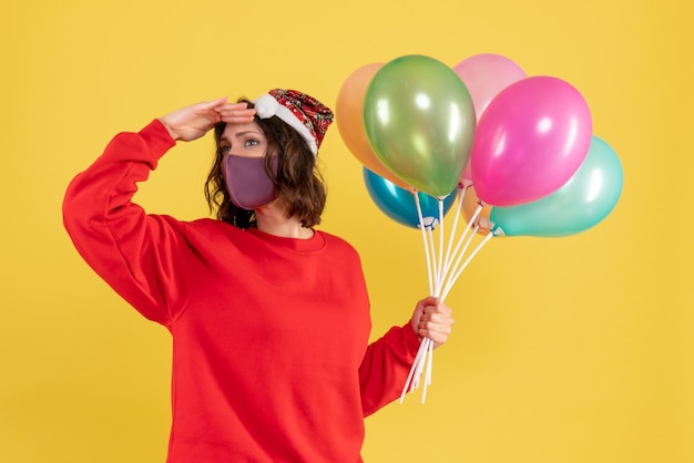 Front view young female holding balloons in sterile mask on yellow 