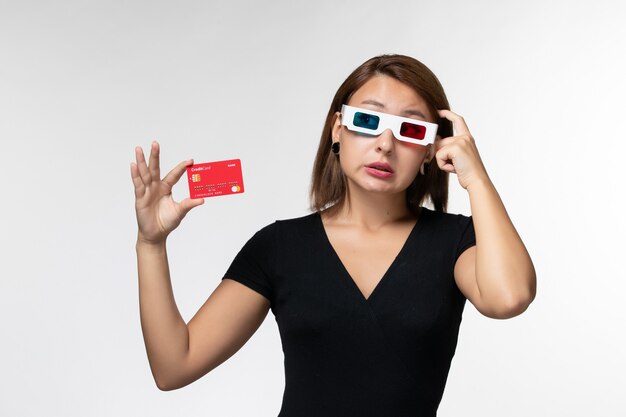 Front view young female holding bank card in d sunglasses and thinking on a white surface