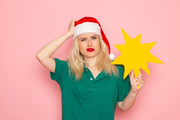 Front view young female holding big yellow figure on pink wall holiday photo new year courier uniform job work