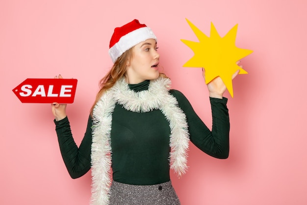 Free photo front view young female holding big yellow figure and sale writing on pink wall color model holiday christmas new year emotions