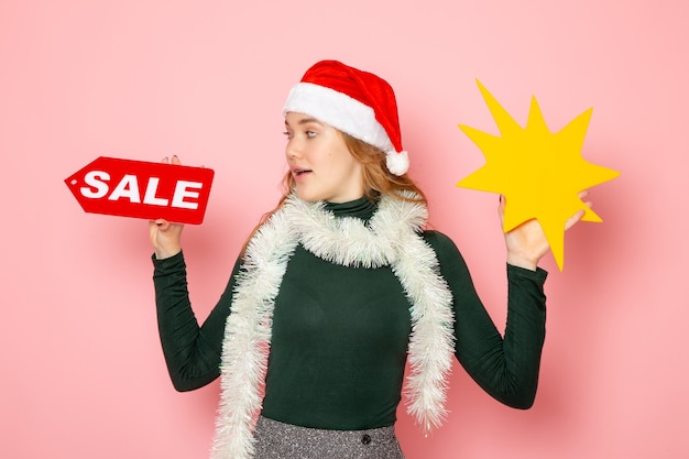 Free photo front view young female holding big yellow figure and sale writing on pink wall color model holidays christmas new year emotion