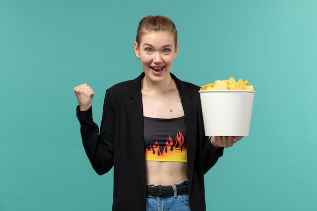 Free Photo front view young female holding chips and watching movie on the blue surface