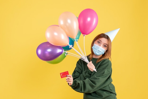 Front view young female holding colorful balloons and bank card