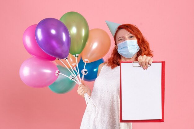 Front view young female holding colorful balloons and file note in mask on pink 