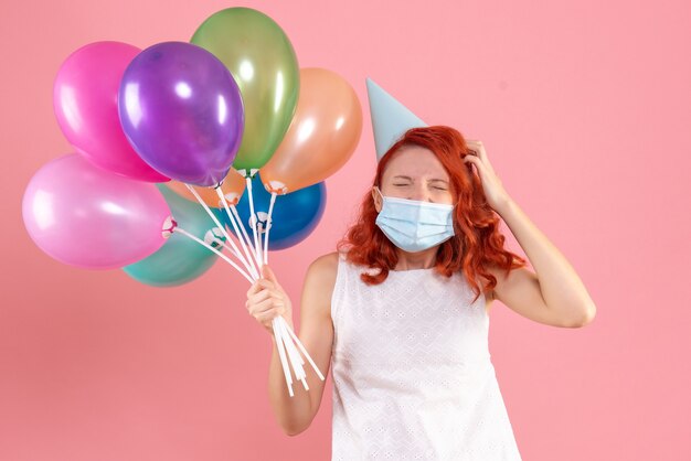 Front view young female holding colorful balloons in mask on pink 