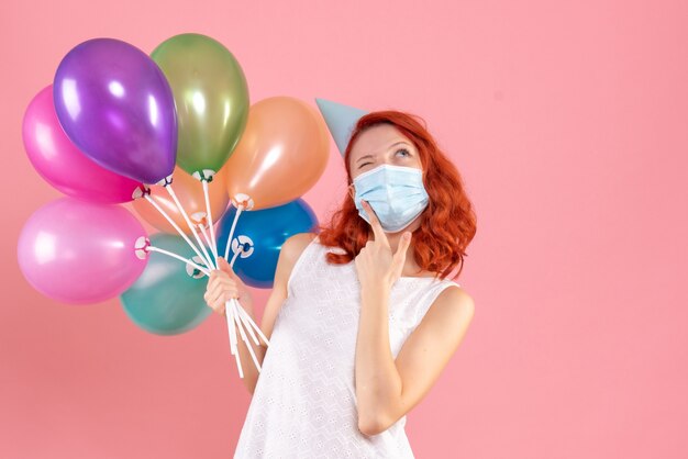 Front view young female holding colorful balloons in mask on pink 