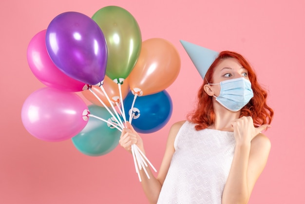 Front view young female holding colorful balloons in mask on pink 