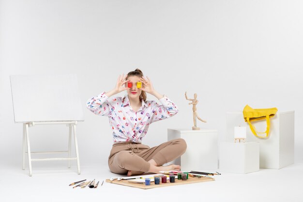 Front view young female holding colorful paints inside cans on white background