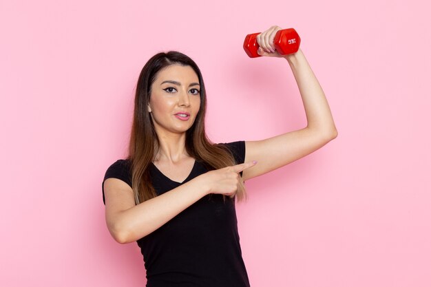 Front view young female holding dumbbells on light pink wall athlete sport exercise health workout