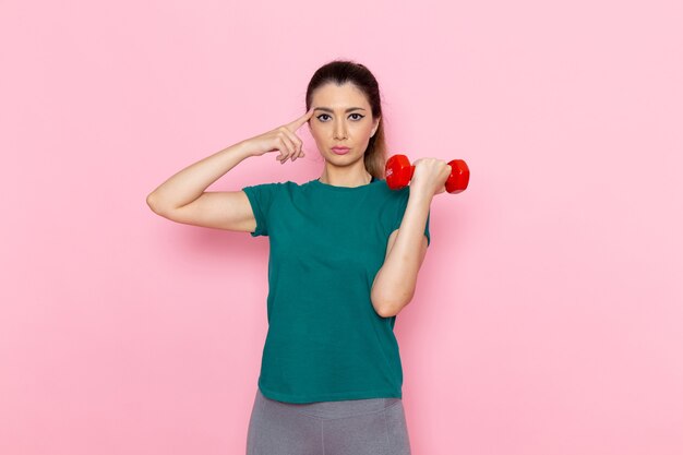 Front view young female holding dumbbells on light-pink wall athlete sport exercise health workouts