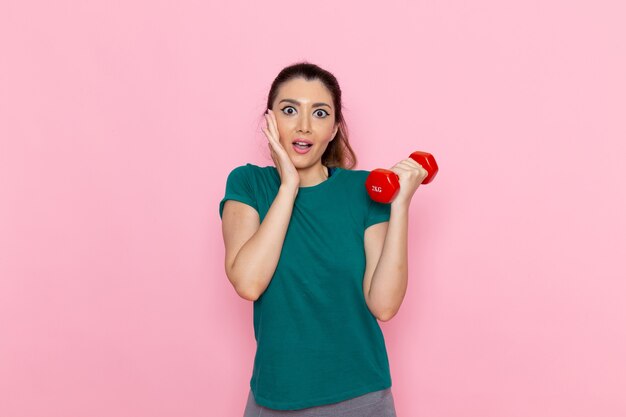 Front view young female holding dumbbells on light pink wall athlete sport exercise health workouts