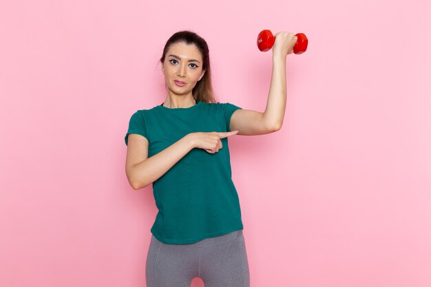 Front view young female holding dumbbells on the light pink wall athlete sport exercise health workouts