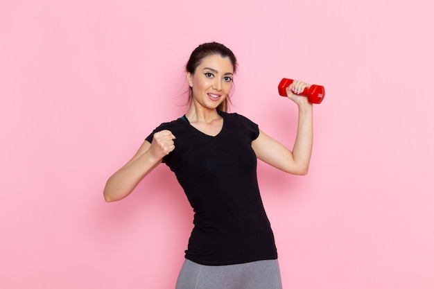 Front view young female holding dumbbells and smiling on light-pink wall athlete sport exercise health workout