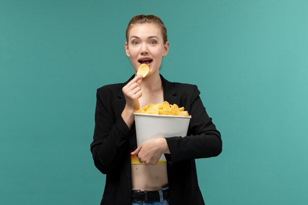 Front view young female holding and eating chips watching movie on the blue surface