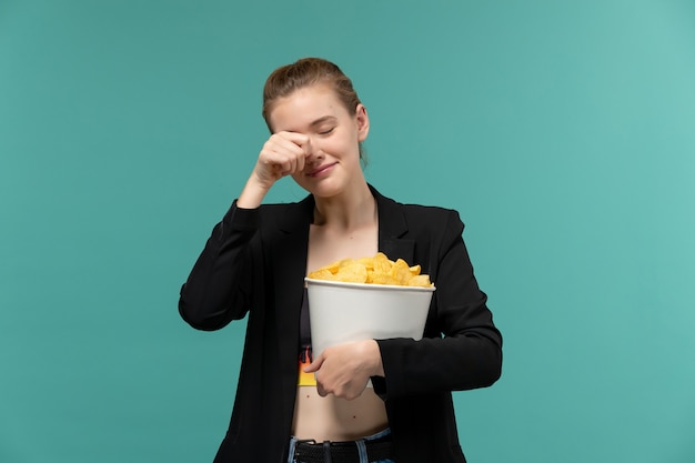 Front view young female holding and eating chips watching movie crying on blue surface