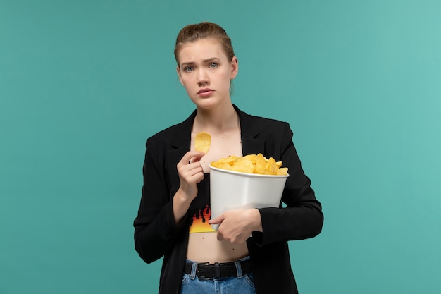 Front view young female holding and eating chips watching movie on light-blue surface