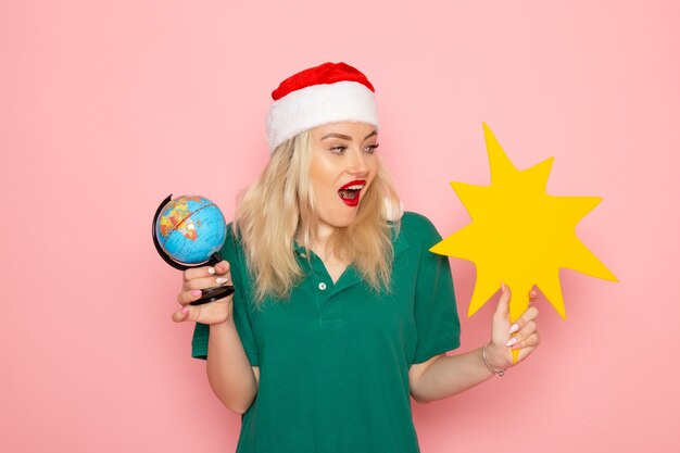 Front view young female holding globe and yellow figure on pink wall model woman xmas holiday photo new year color