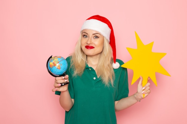 Free photo front view young female holding globe and yellow figure on pink wall model woman xmas holiday photo new year color