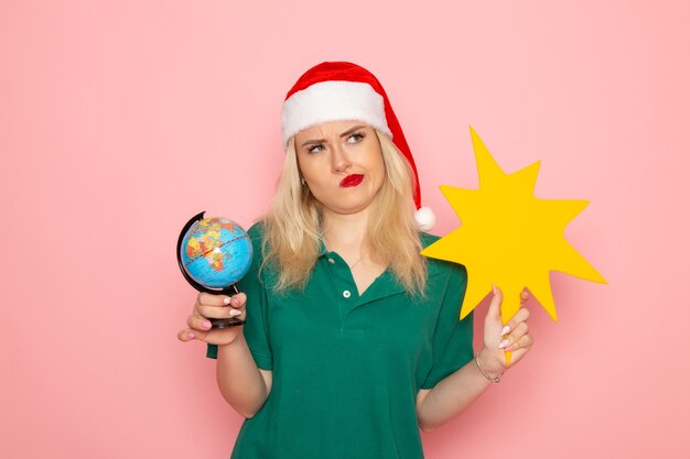 Front view young female holding globe and yellow figure on pink wall model woman xmas holiday photo new year colors