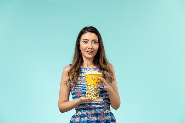 Front view young female holding popcorn package on blue surface