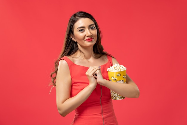 Free Photo front view young female holding popcorn on red surface