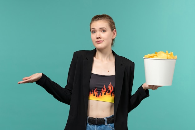 Free Photo front view young female holding potato chips and watching movie on blue desk