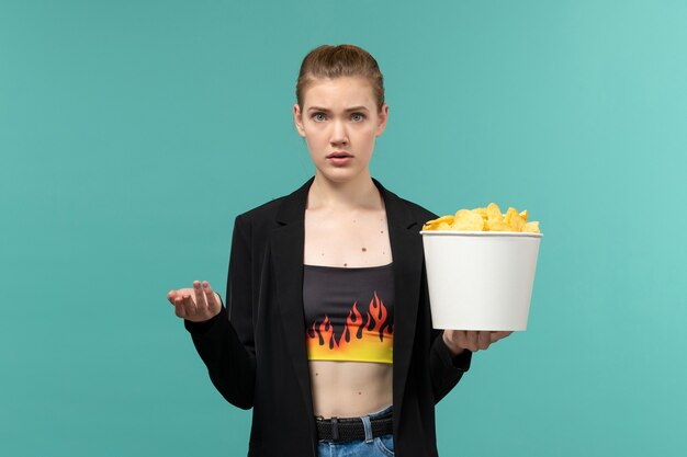 Front view young female holding potato chips and watching movie on the blue desk