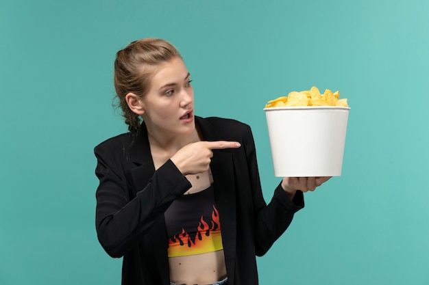 Free Photo front view young female holding potato chips and watching movie on blue surface