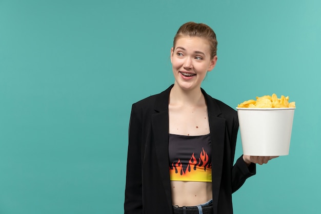 Front view young female holding potato chips and watching movie on blue surface