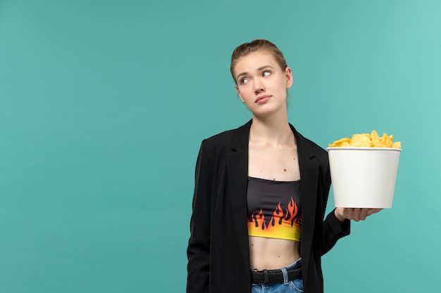 Front view young female holding potato chips and watching movie on light-blue surface