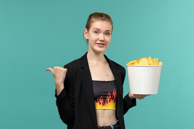 Front view young female holding potato chips and watching movie on light blue surface