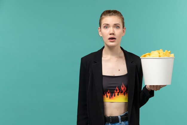 Front view young female holding potato chips and watching movie on light blue surface