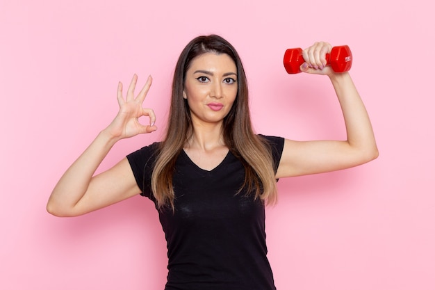 Front view young female holding red dumbbells on light pink wall athlete sport exercise health workout