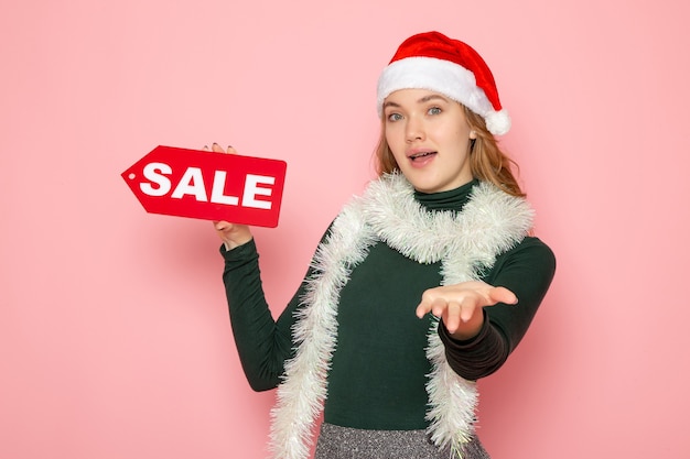 Free photo front view young female holding red sale writing on pink wall christmas holiday new year shopping fashion emotion