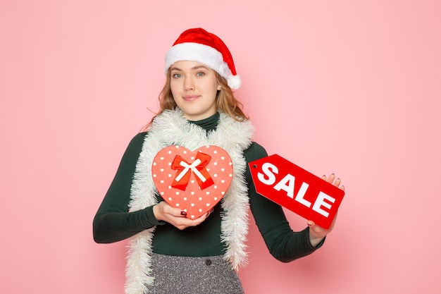 Free photo front view young female holding red sale writing on pink wall new year shopping fashion emotion holiday