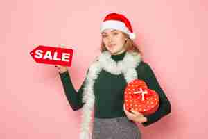 Free photo front view young female holding red sale writing and present on pink wall christmas new year shopping emotion holiday colors