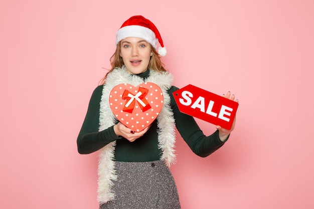 Free Photo front view young female holding red sale writing and present on pink wall christmas new year shopping fashion emotions holiday