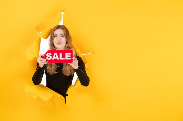 Free Photo front view young female holding red sale writing on yellow ripped wall