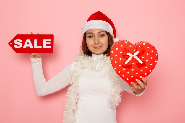 Free photo front view young female holding sale writing and present on pink wall color holiday new year fashion snow christmas